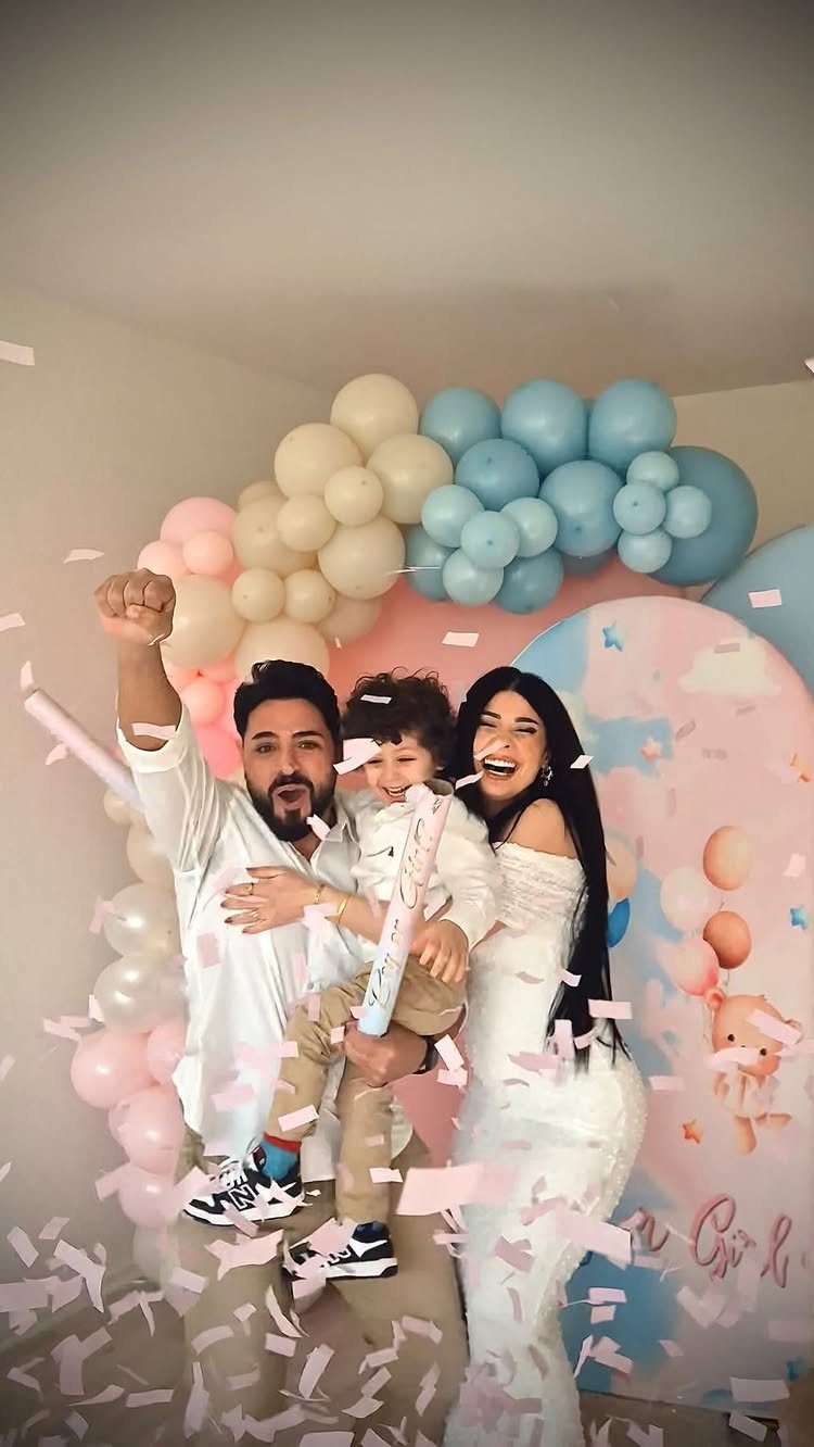 Family in white clothes celebrating with pink confetti and pastel balloon decorations.