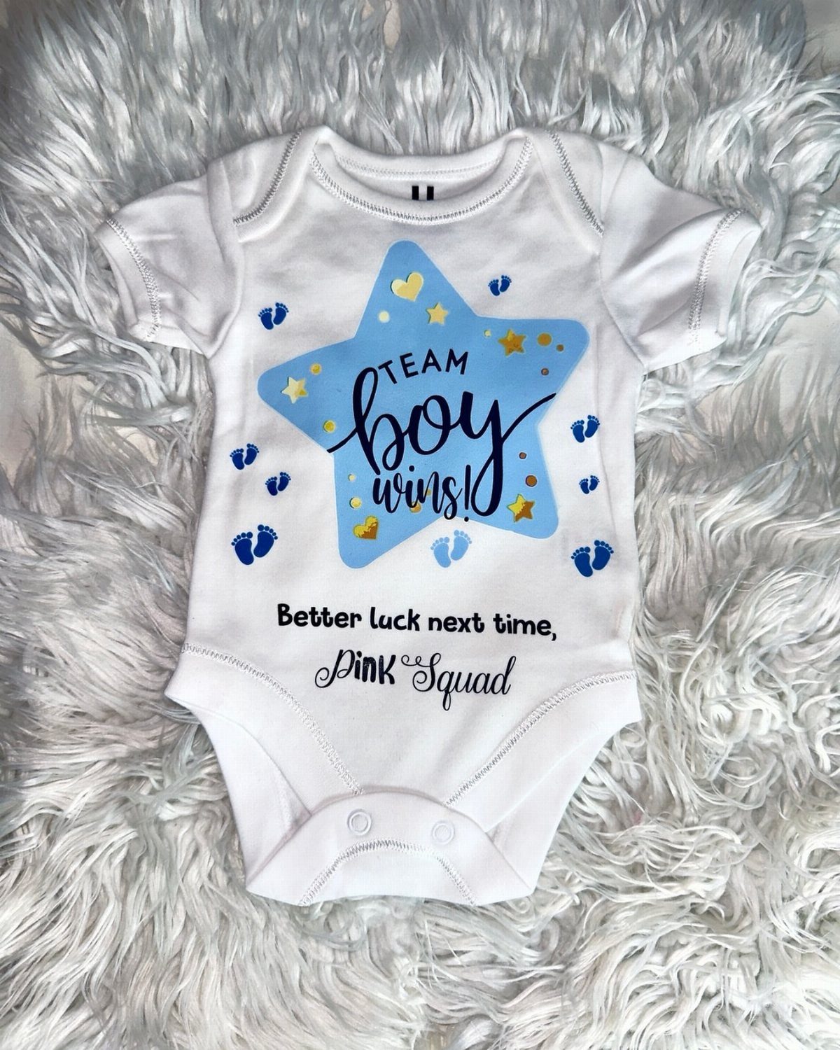 White baby onesie with blue star and Team Boy text on white fur.