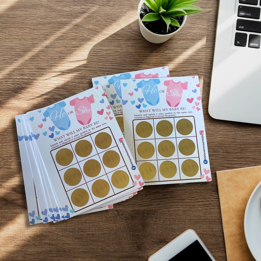 Gender reveal scratch-off cards with gold circles on a wooden table next to a plant.