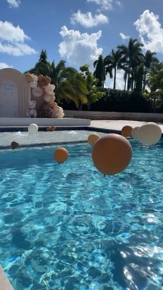 Floating tan and white balloons in a pool with a neutral balloon arch background.