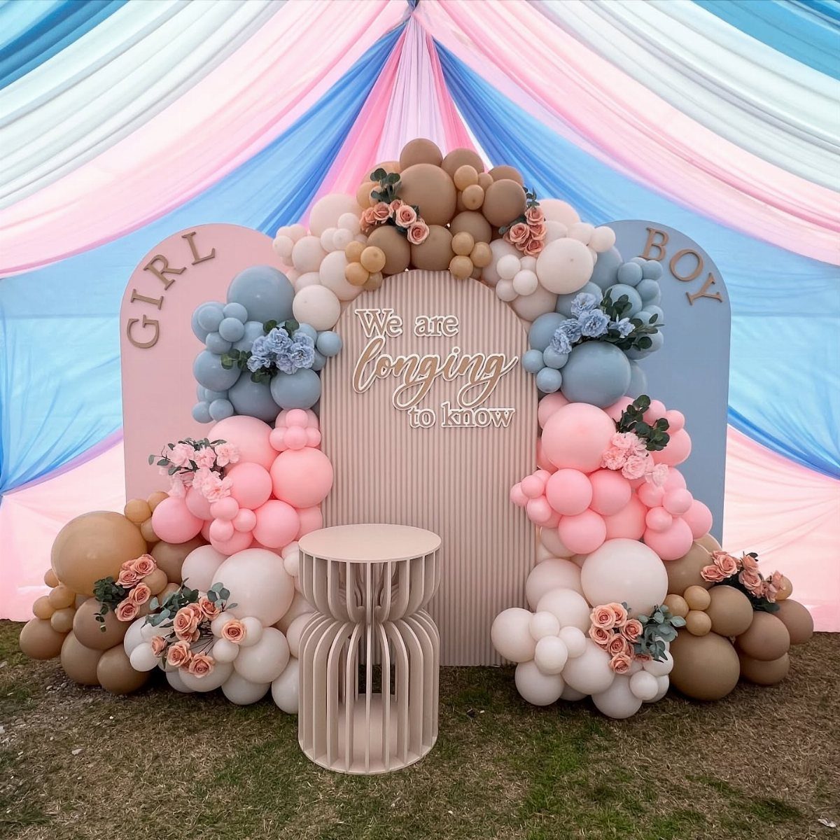 Gender reveal party setup with pink and blue balloons, floral accents, and draped fabric.