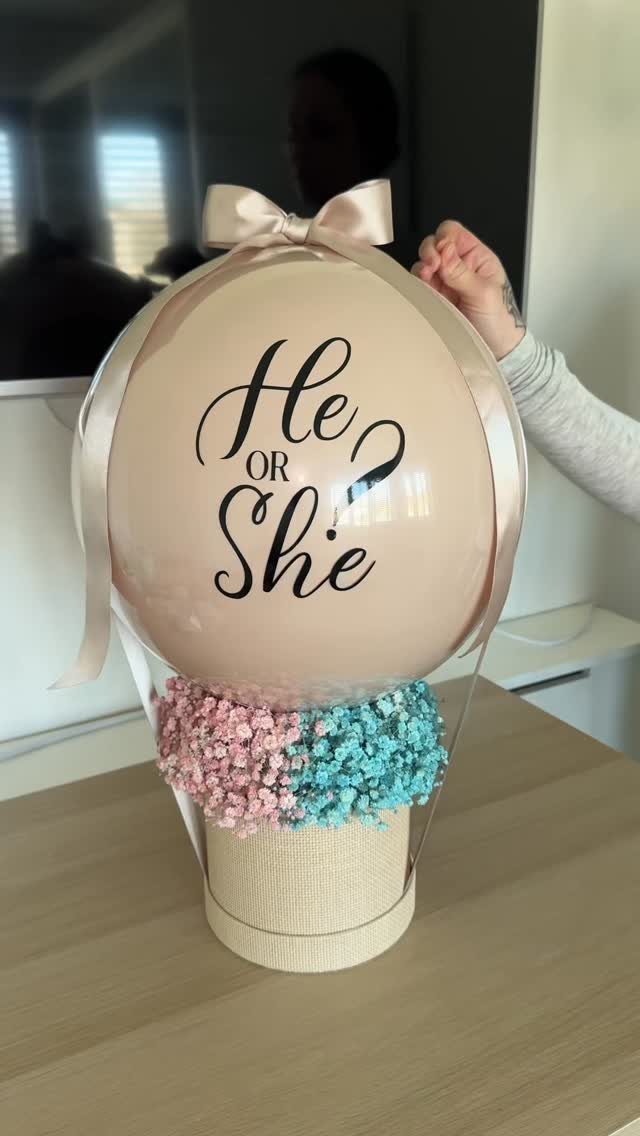 Gender reveal balloon arrangement with He or She text and pink and blue flowers