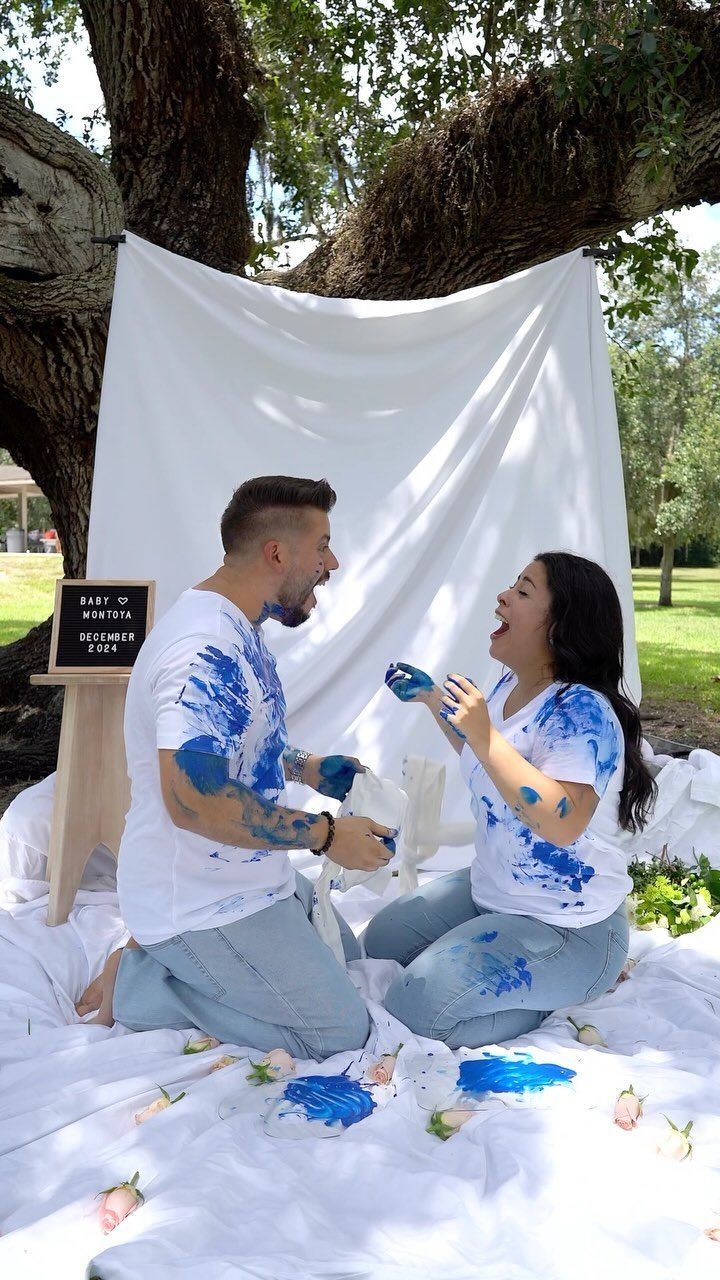 Couple covered in blue paint sitting on a white sheet for gender reveal.