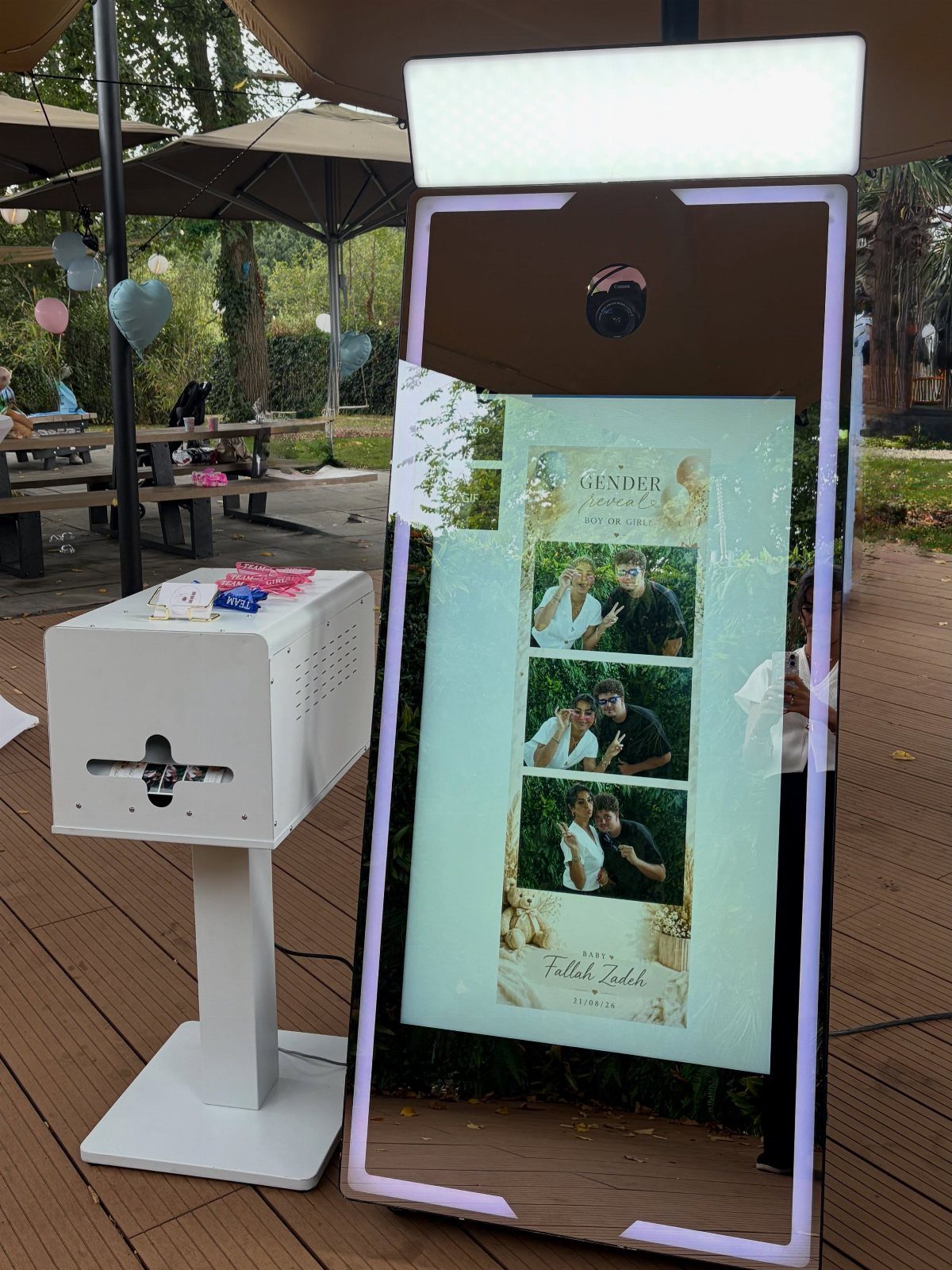 Mirror photo booth displaying a couple's photo strip on a wooden outdoor deck.