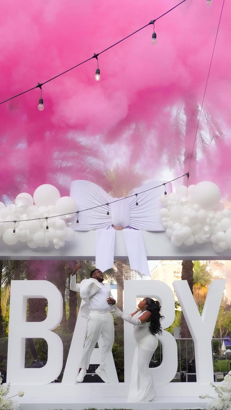Couple in white celebrating with a large pink smoke cloud and BABY letters.