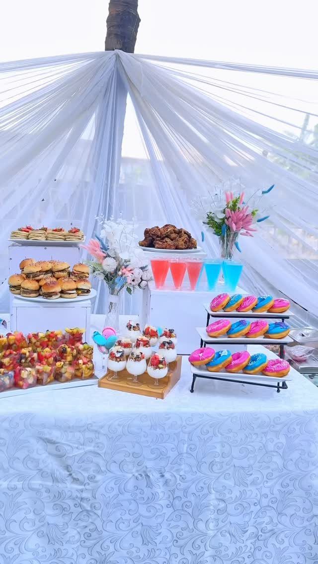 Dessert table with pink and blue themed treats under a white fabric canopy.