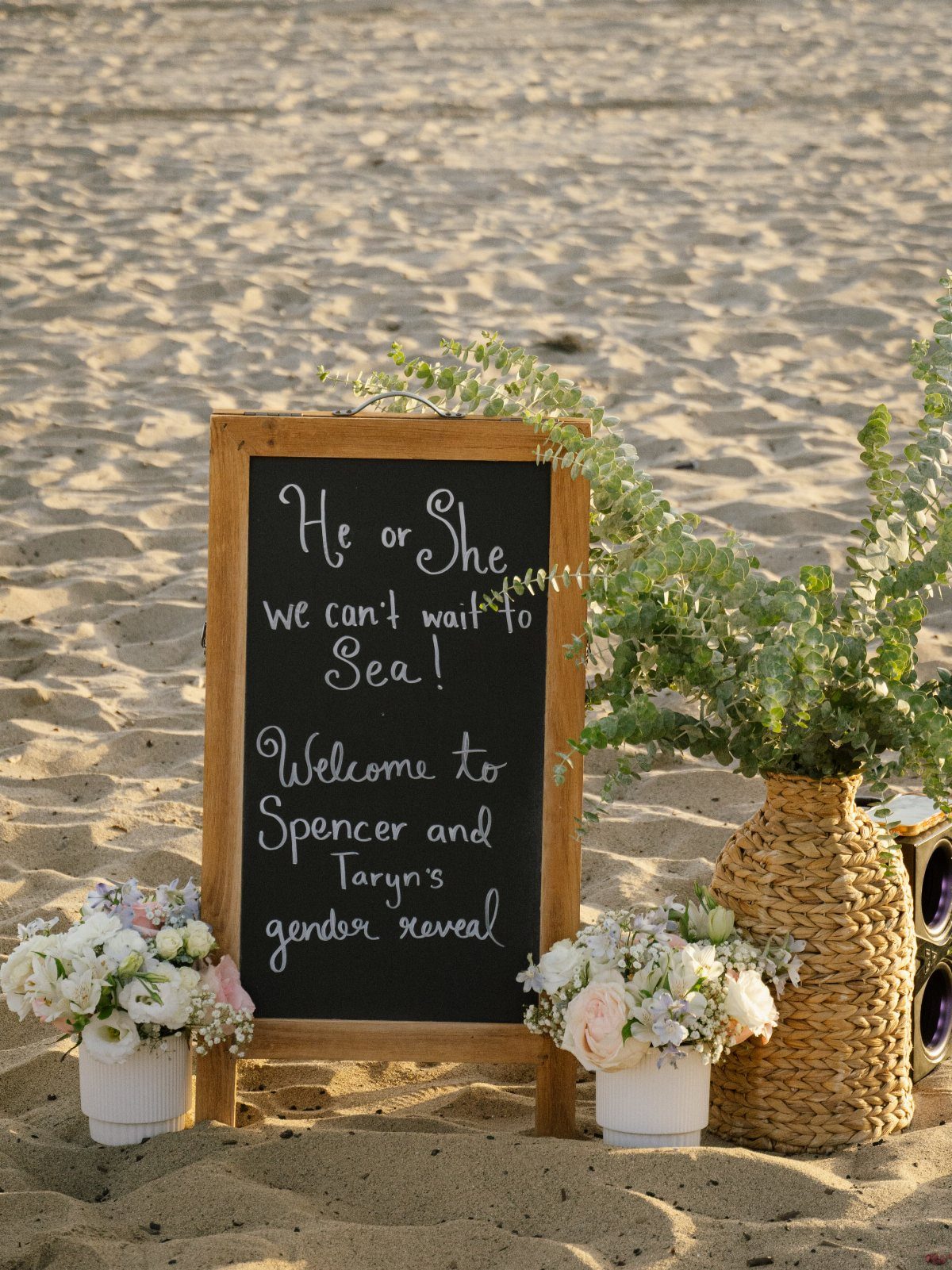 Chalkboard welcome sign for a gender reveal party on a sandy beach.