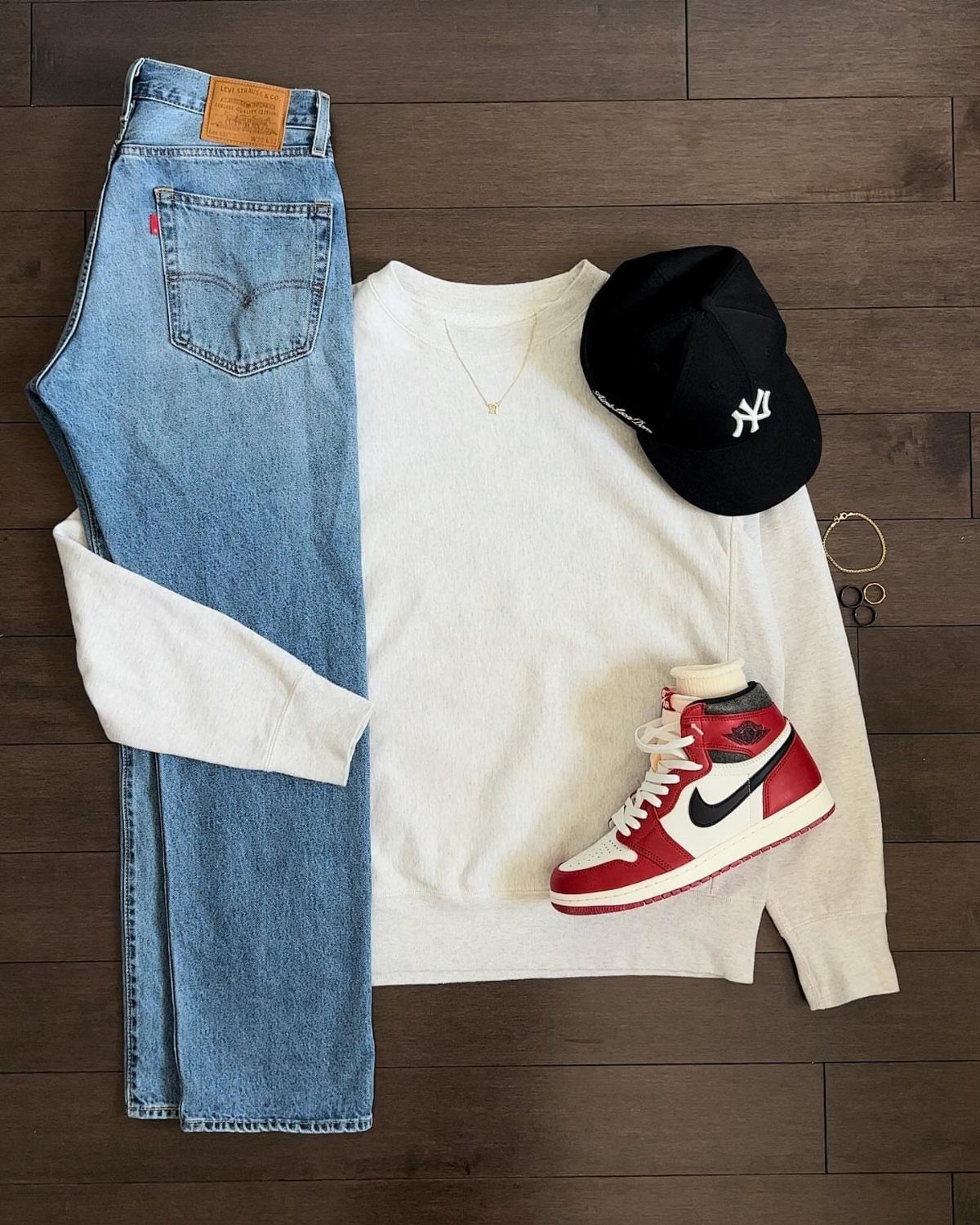 Casual outfit flat lay with blue jeans, white shirt, black cap, and red sneakers.
