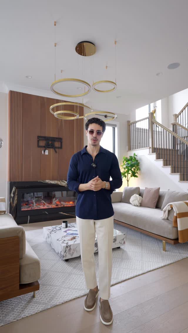 Man in blue button-down shirt and white trousers posing in a modern living room
