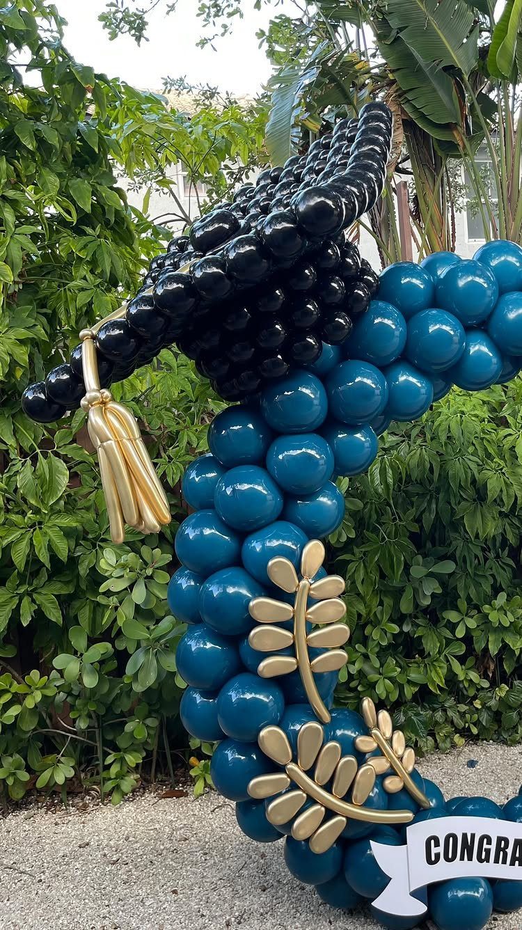 Graduation cap and gown balloon sculpture in teal and black with gold accents.