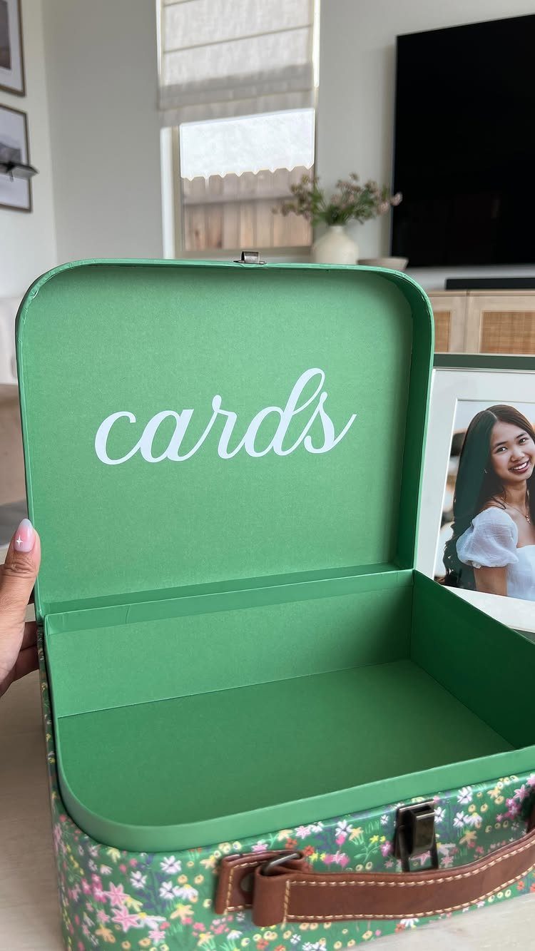 Green floral card box with white script text and a nearby framed photo.