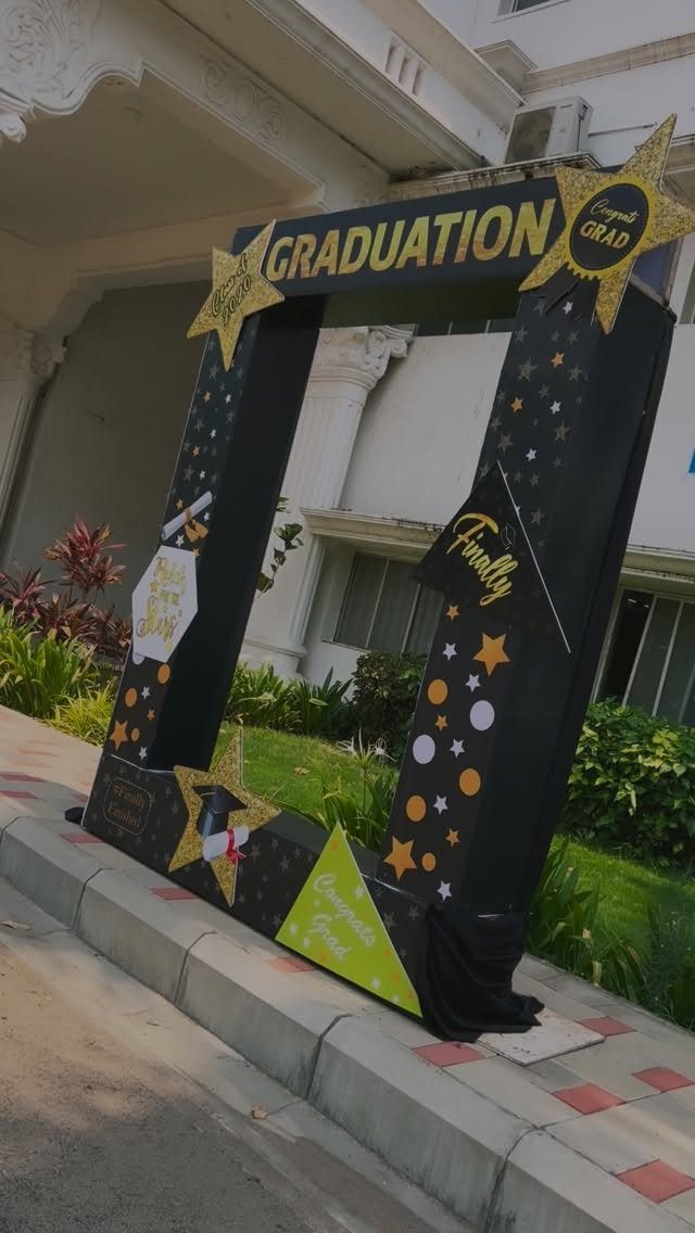 Black graduation photo frame prop with gold stars and graduation text outdoors.