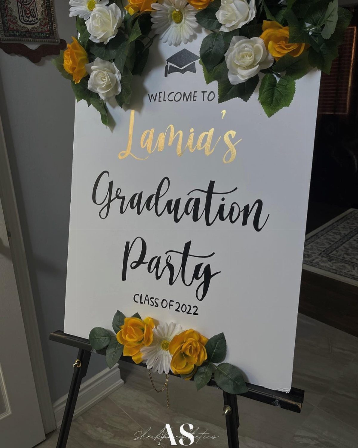 Personalized graduation welcome sign on an easel decorated with yellow and white roses.