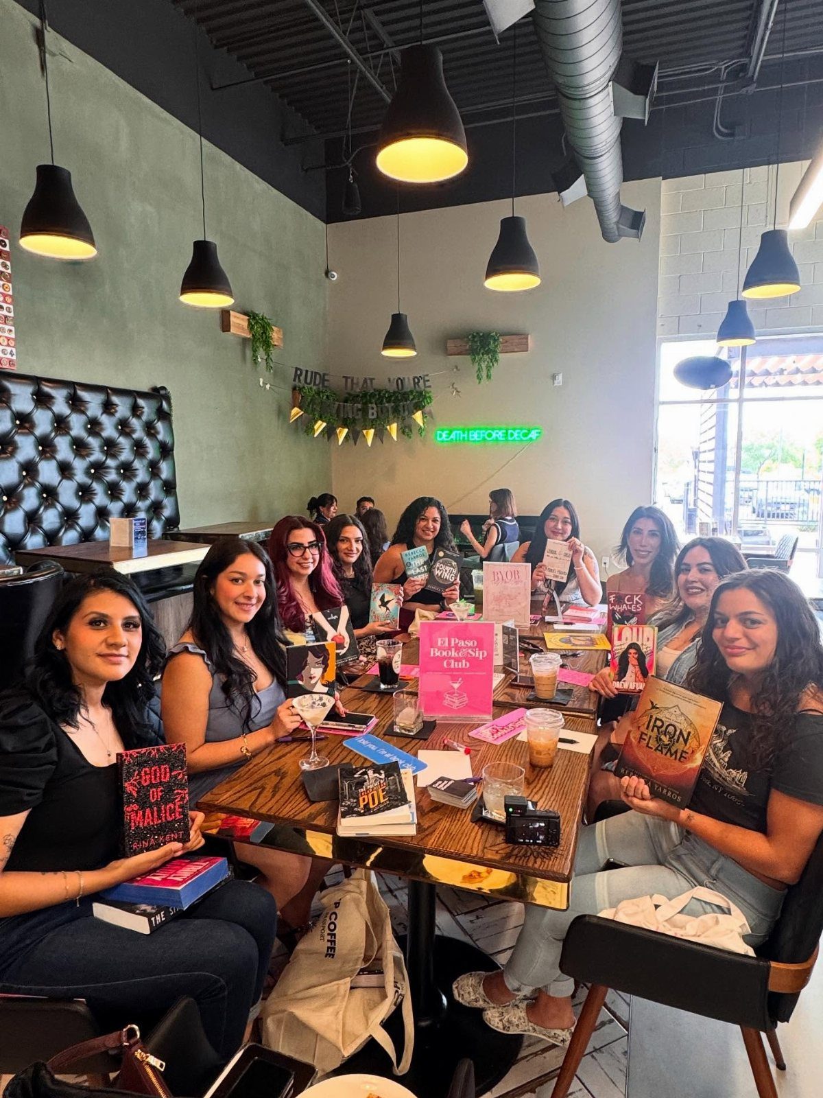 Group of women holding books while sitting at a cafe table for book club.