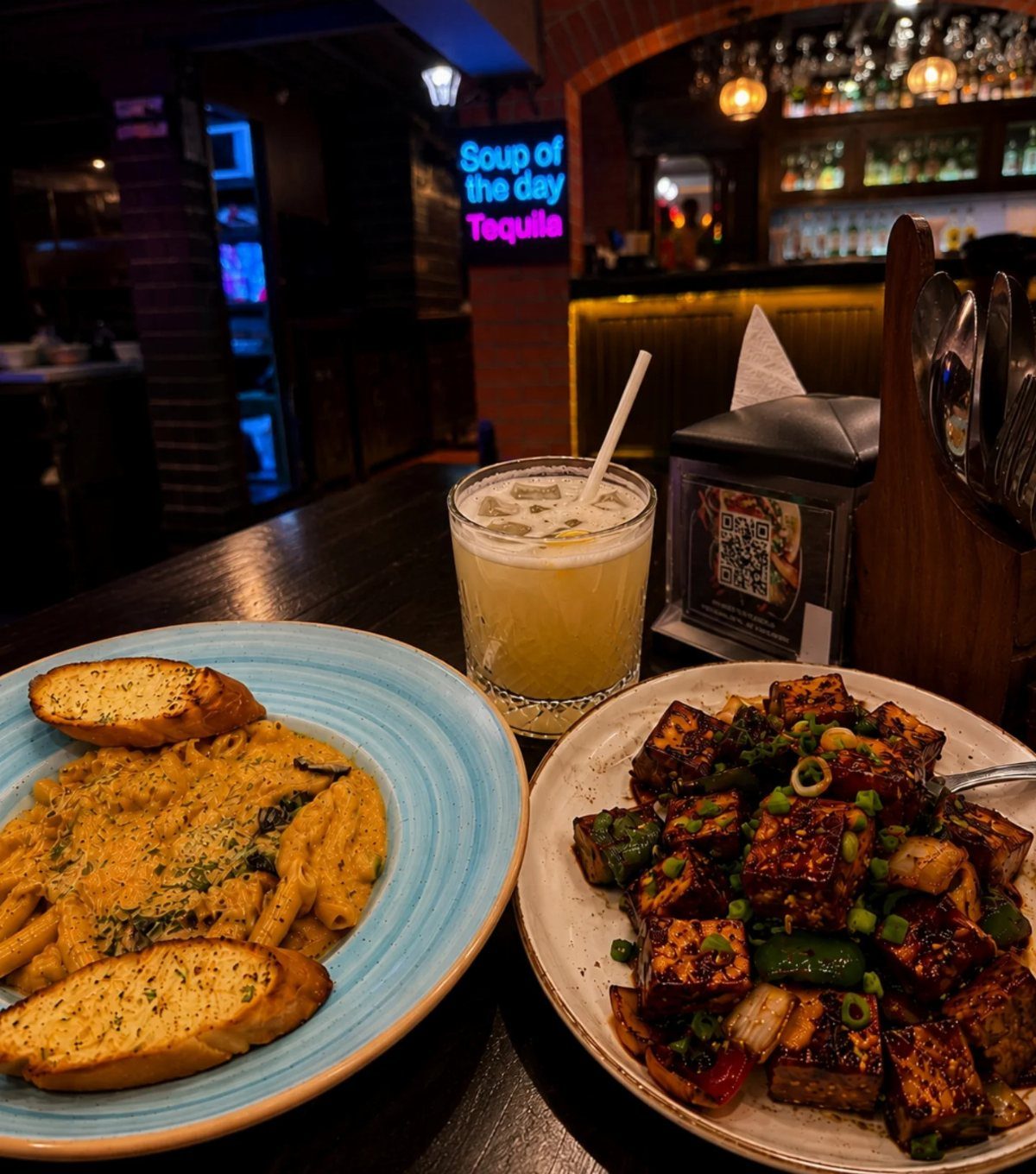 Pasta with garlic bread and tofu dish on a restaurant table with drink.