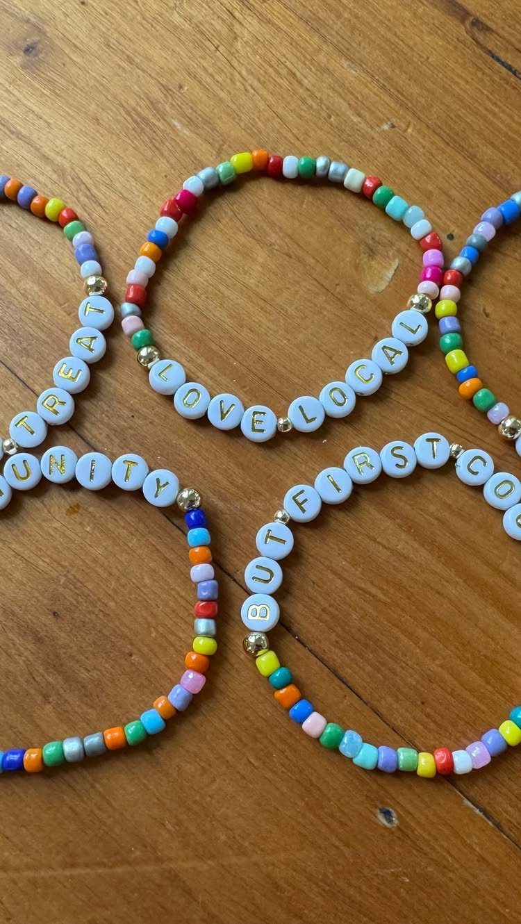 Colorful beaded friendship bracelets with letter beads on a wooden table surface.