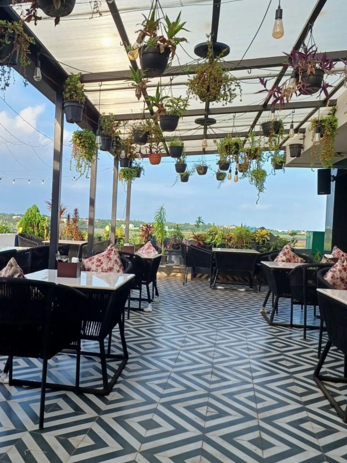 Rooftop patio with black furniture, geometric tiled floors, and hanging green plants.