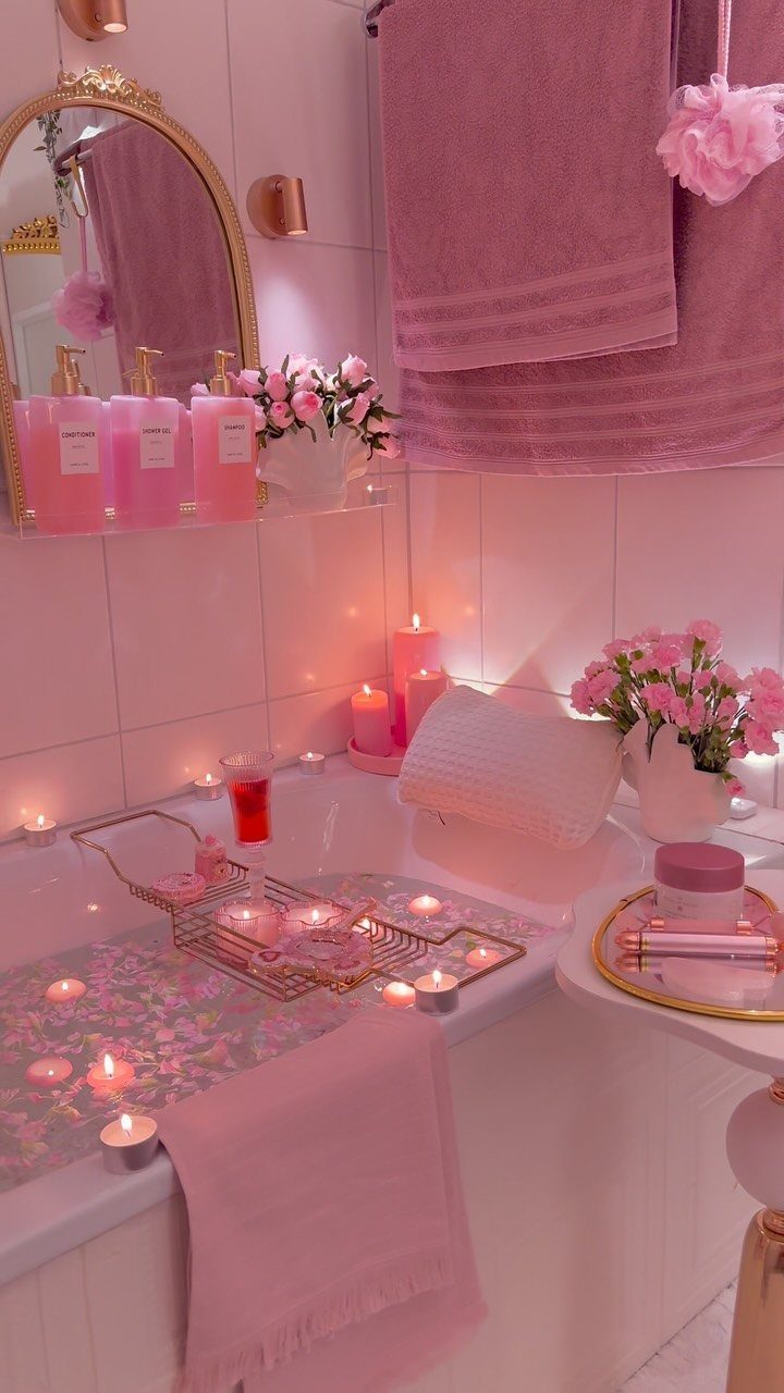 Pink themed bathroom with a bathtub, lit candles, and pink towels for pampering.