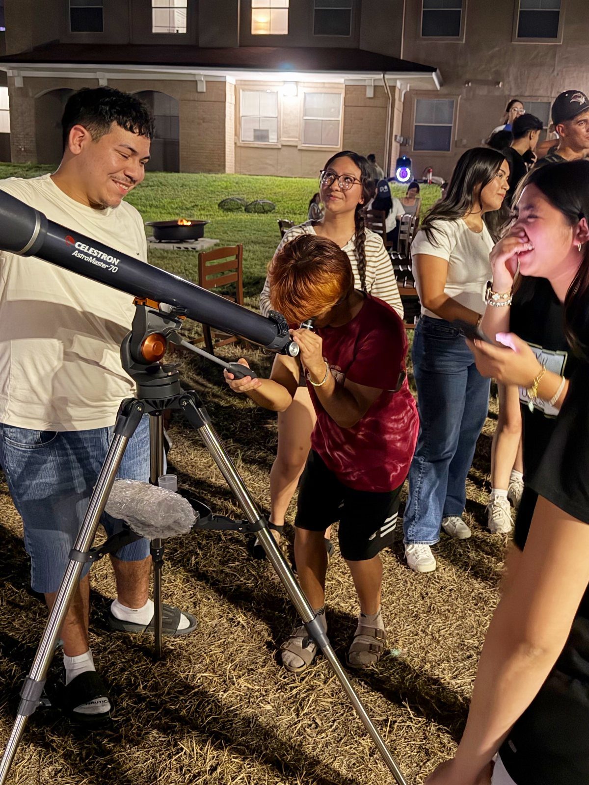 Group of friends using a telescope to look at the night sky outdoors.