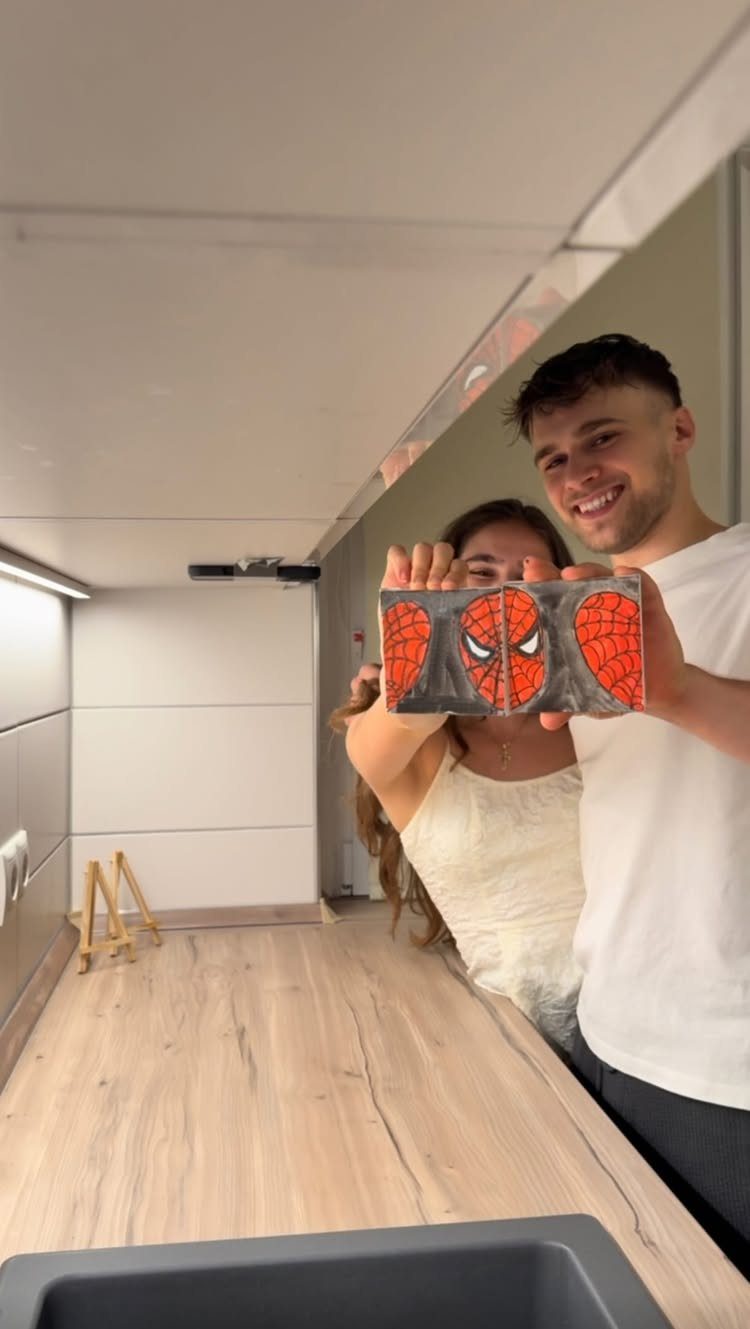Couple holding a handmade Spider-Man painting in a modern white room.