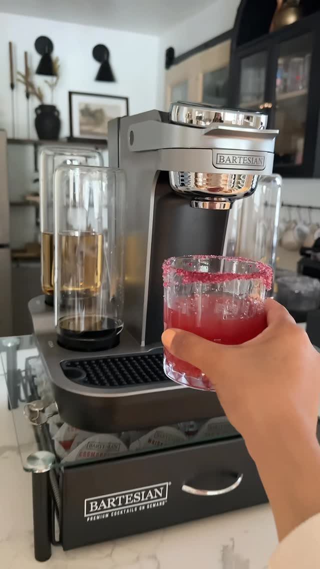Red cocktail with salted rim held in front of a cocktail machine.