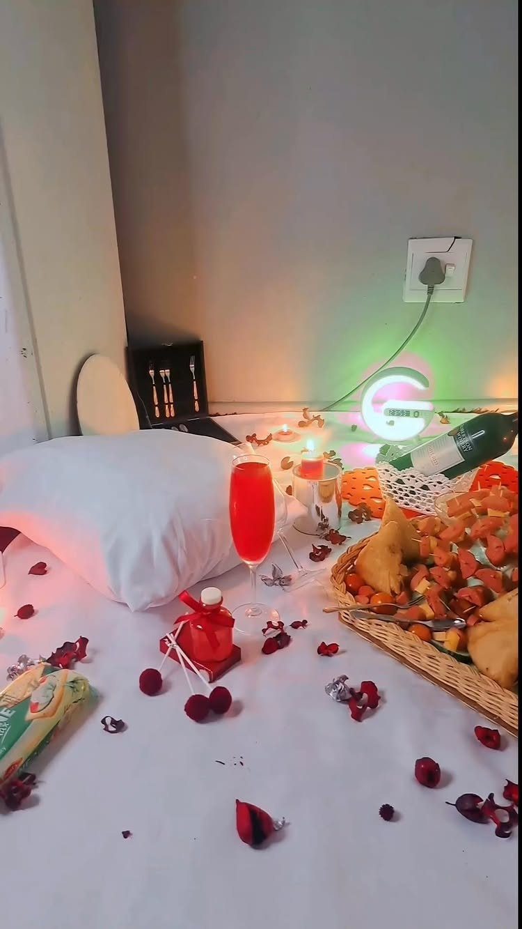 Romantic indoor picnic setup with food basket, wine, and red rose petals.