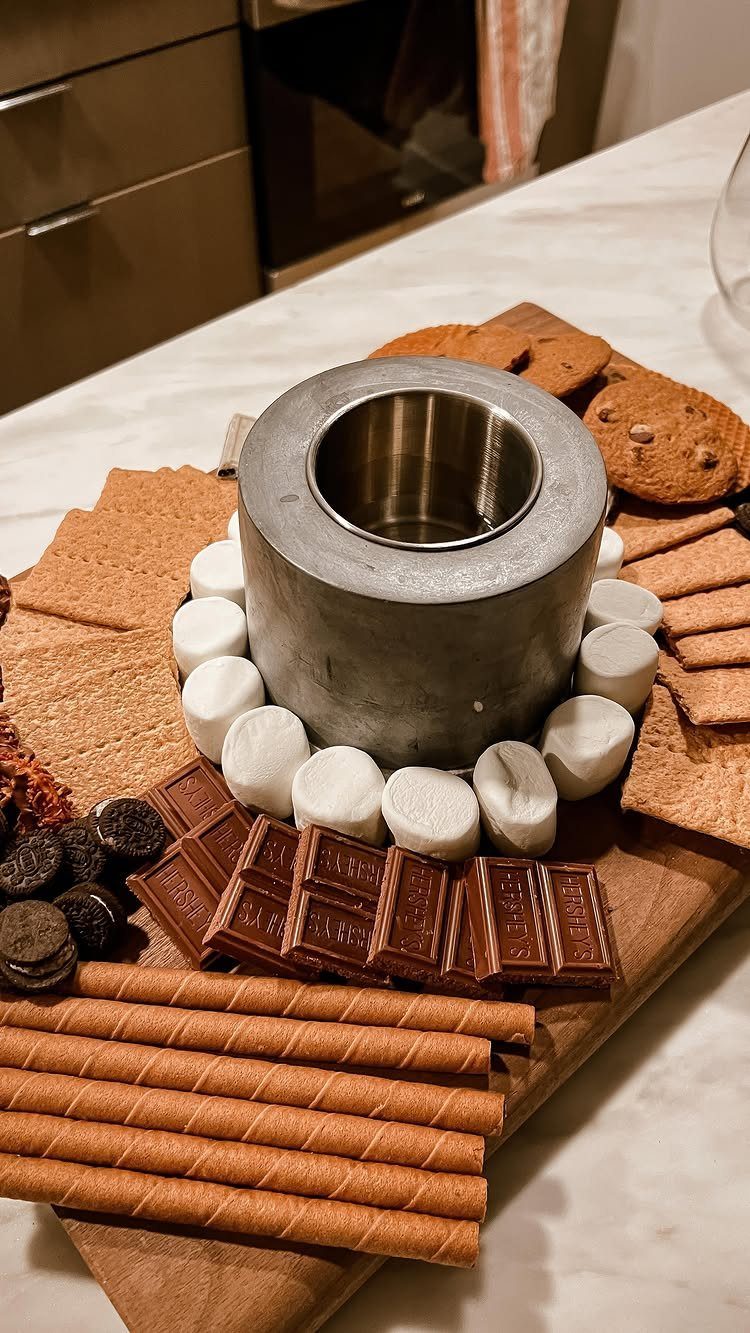 S'mores platter with a metal heater, marshmallows, chocolate, and graham crackers on wood.