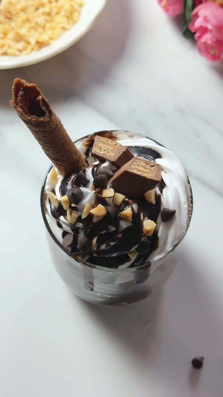 Ice cream sundae with chocolate syrup, nuts, and a wafer roll in glass.