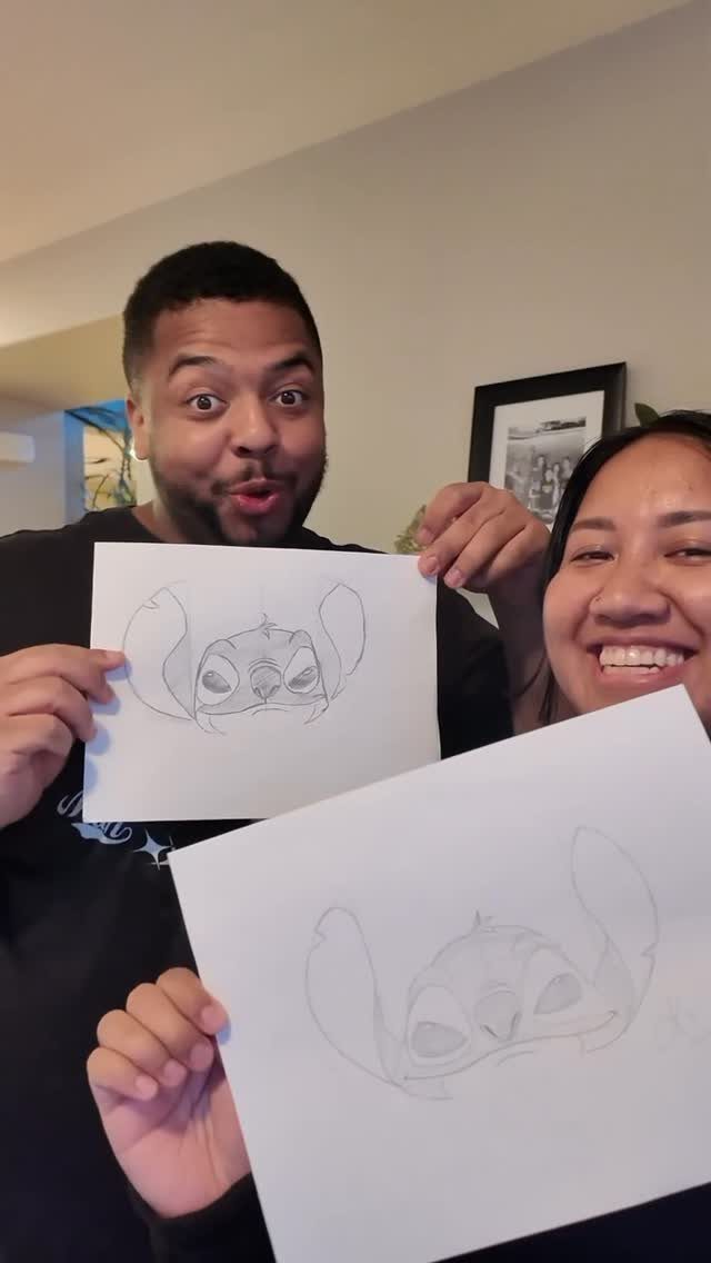 Couple holding up pencil drawings of a cartoon character in their home.