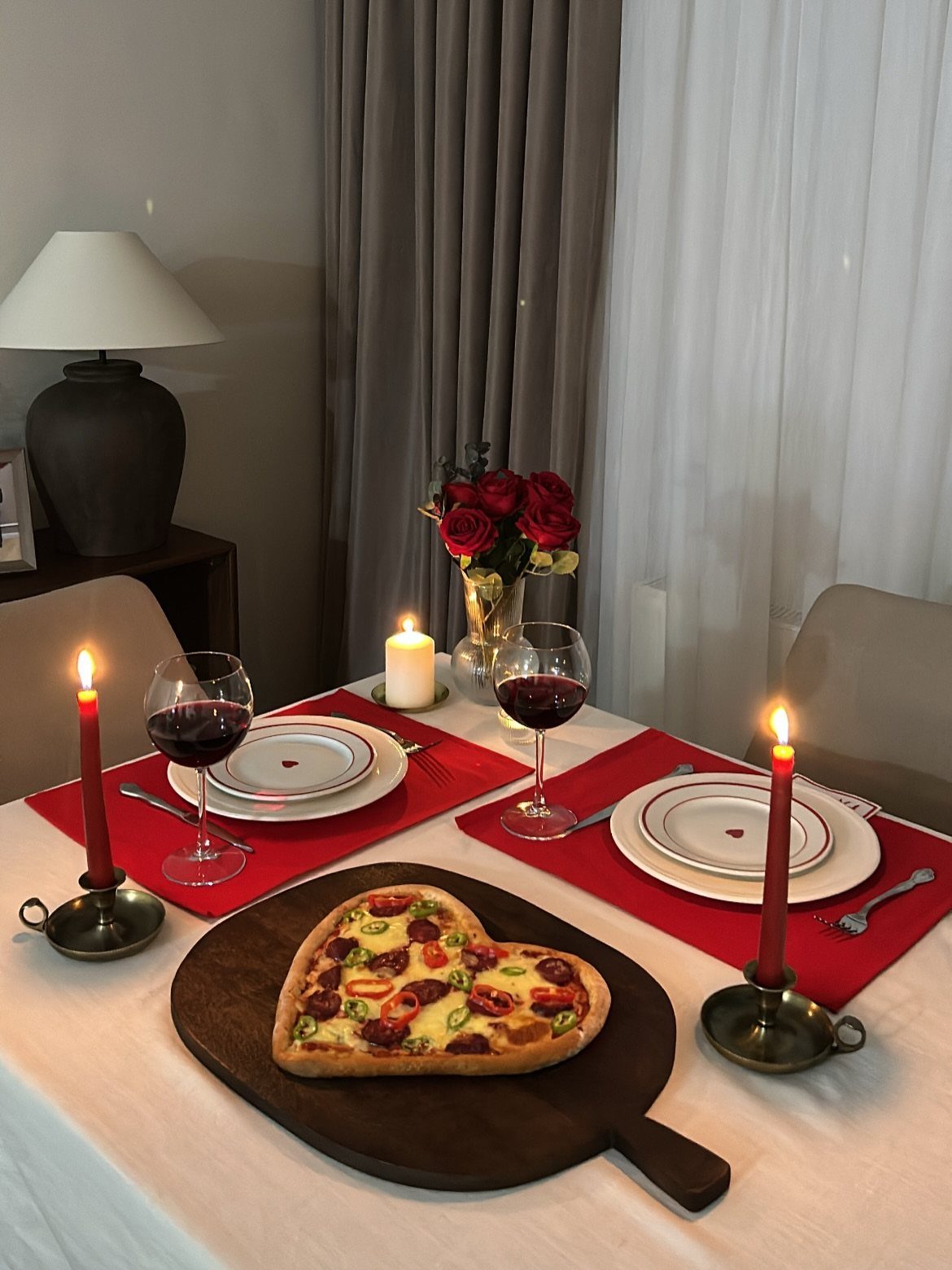 Heart-shaped pizza and red wine on a table set with lit candles.