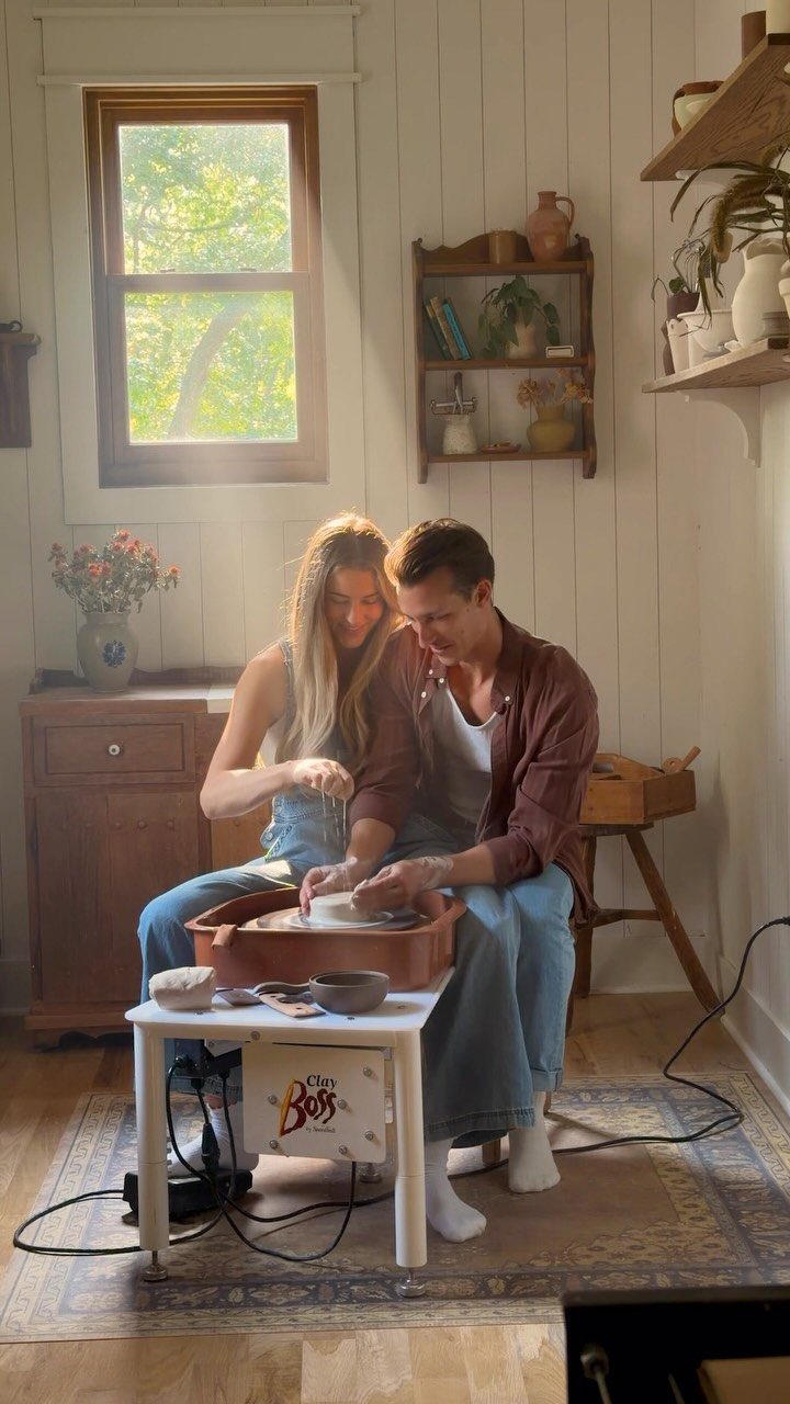Couple using a pottery wheel to shape clay in a rustic home studio.