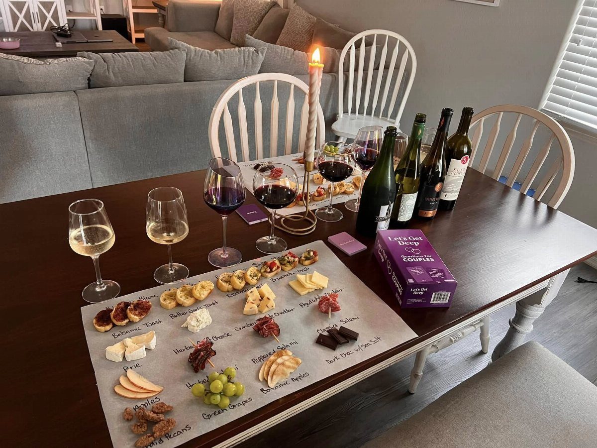 Wine glasses and bottles with a charcuterie board and candle on a table.