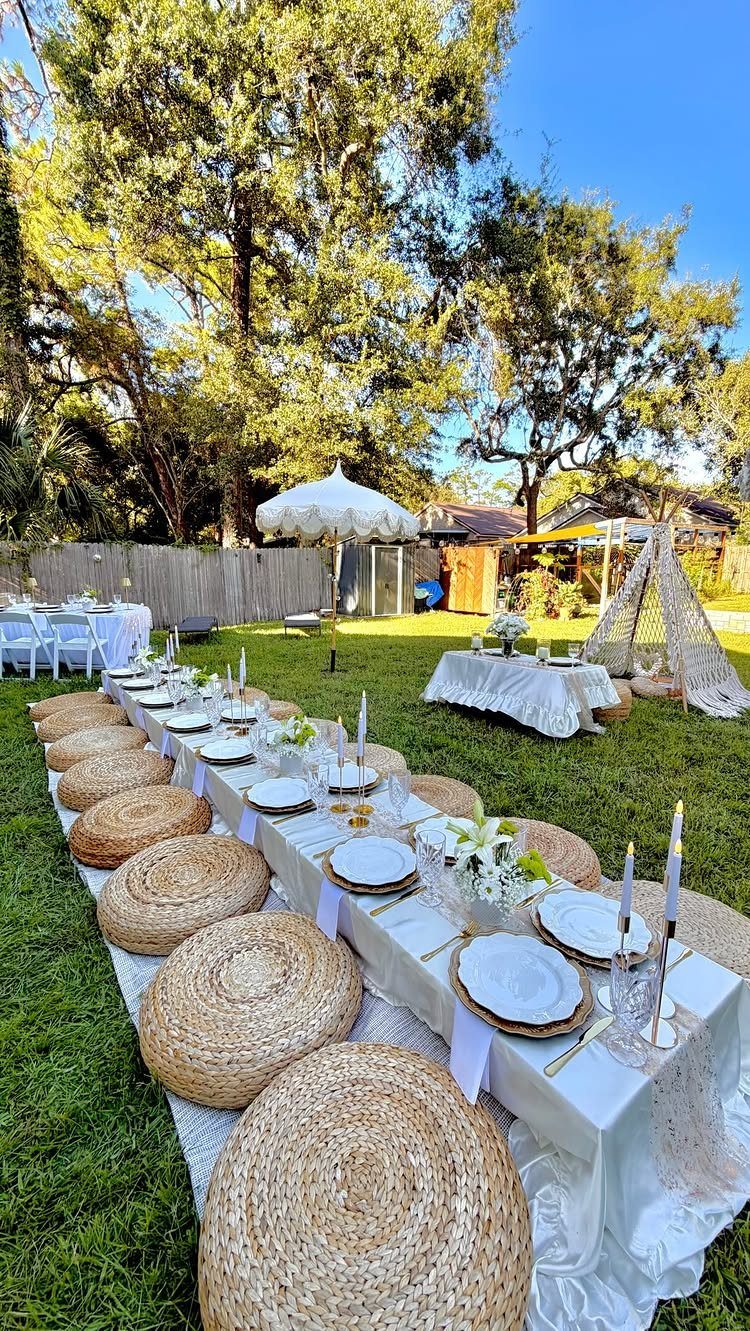 Low white dining table with straw floor cushions set on a sunny green lawn