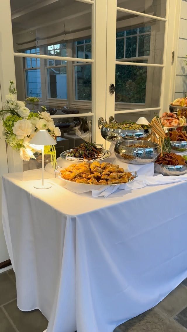 Buffet table with appetizers and white flowers in front of white French doors.