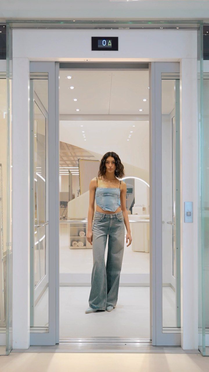 Woman wearing a denim corset top and wide-leg jeans standing in an elevator.