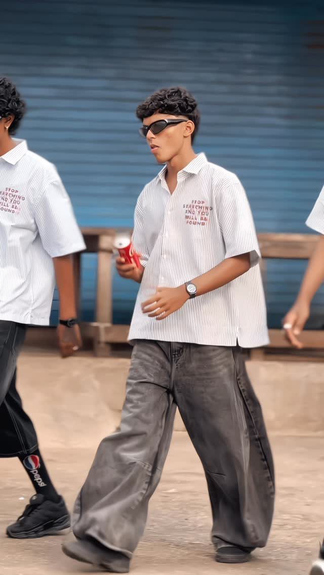 Young man wearing a white button-down shirt and wide-leg grey trousers walking outdoors.
