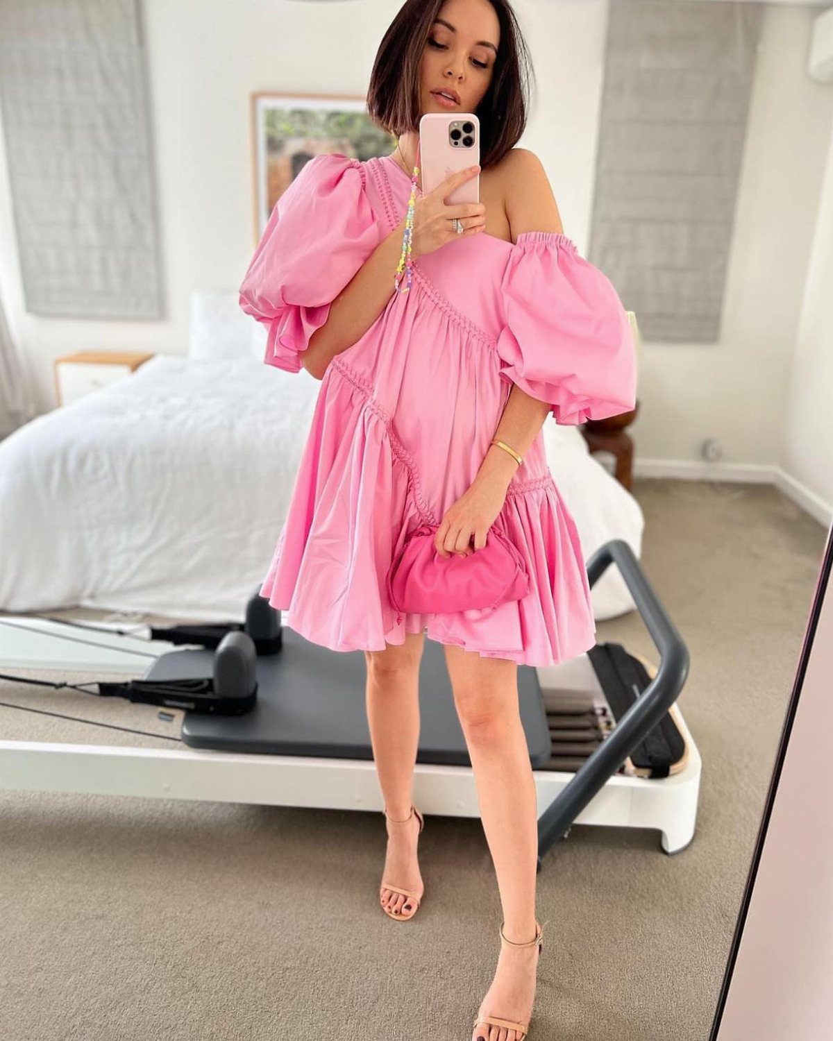 Woman in a pink puff-sleeve mini dress and nude heels taking a selfie.