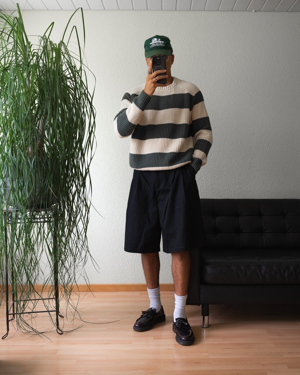 Person wearing a striped sweater and tailored shorts posing in a living room.