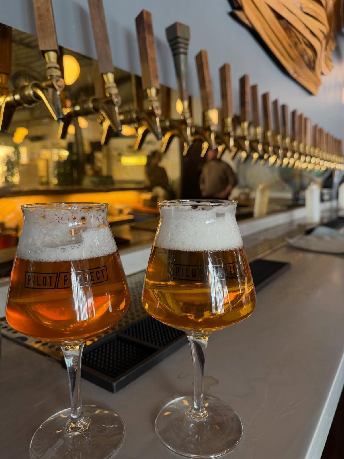Two glasses of craft beer on a bar counter with beer taps behind.