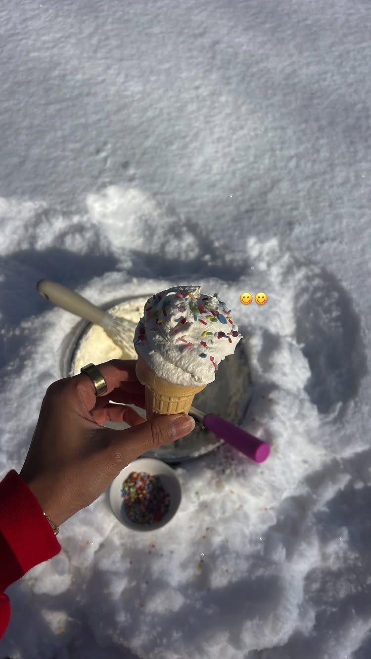 Snow ice cream in a waffle cone with sprinkles held over fresh snow.