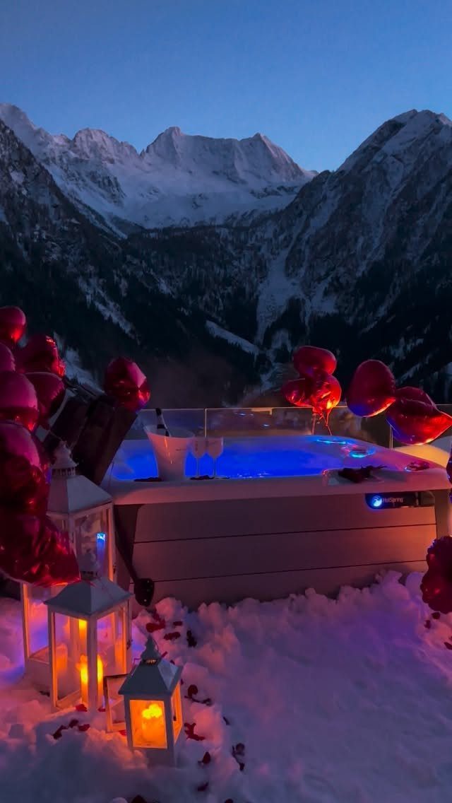 Glowing blue hot tub with red heart balloons and lanterns in snowy mountains