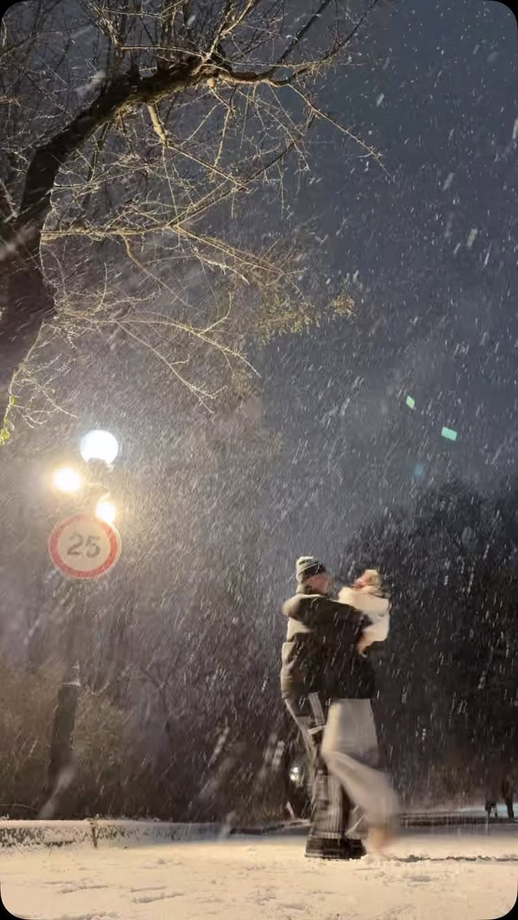 Couple embracing and dancing in the falling snow at night under a street lamp.