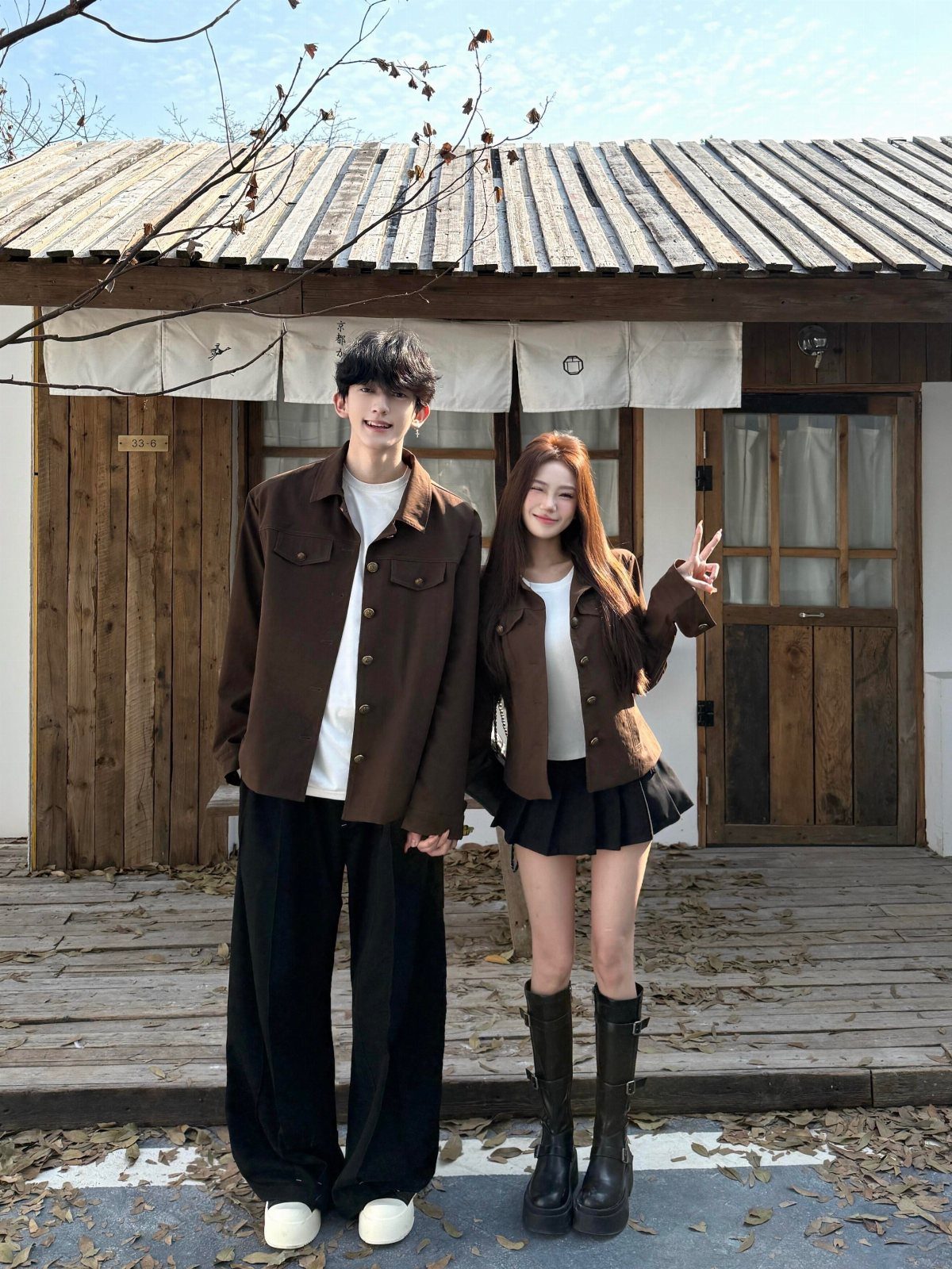 Couple posing in matching brown jackets, white shirts, and black bottoms outdoors.
