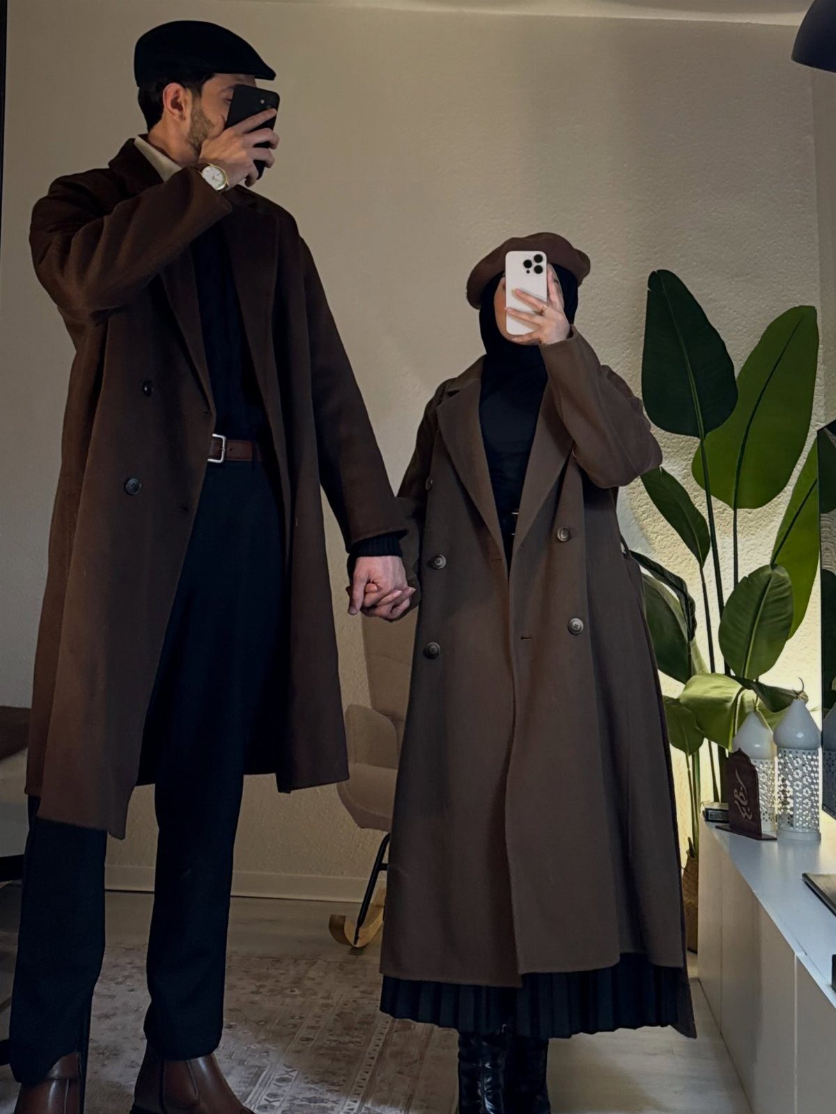 Couple wearing matching long brown wool coats over black turtlenecks and brown hats.
