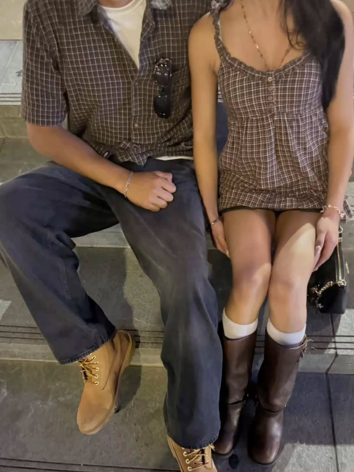 Couple wearing matching brown plaid button-down outfits sitting together outdoors.