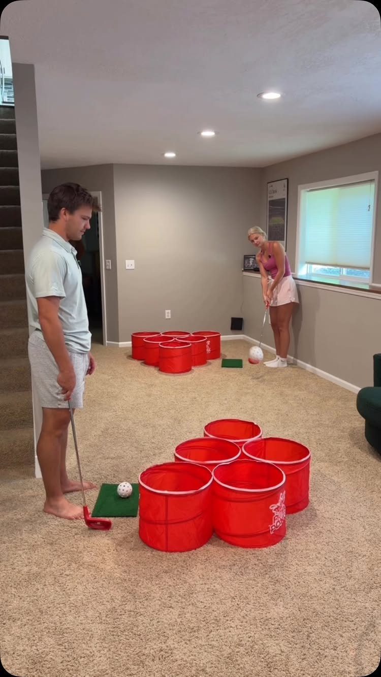 Man and woman playing homemade mini golf with red buckets in a living room