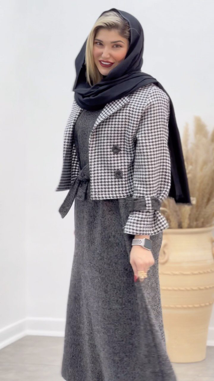 Woman in black hijab, houndstooth jacket, and long grey skirt standing indoors.