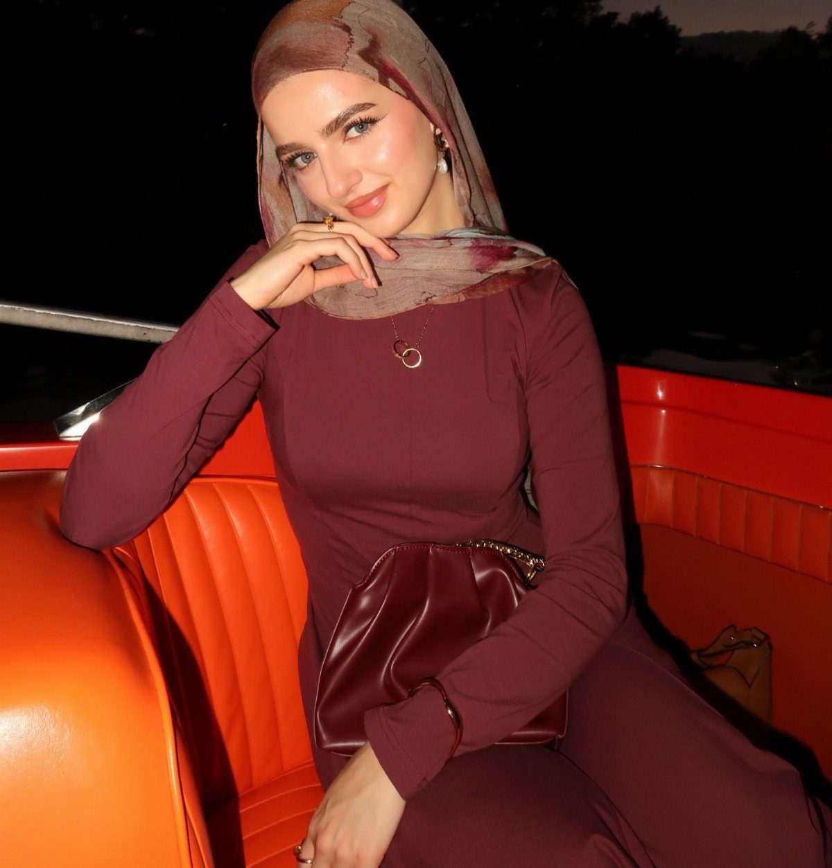 Woman in maroon long-sleeve dress and hijab sitting in vintage red car