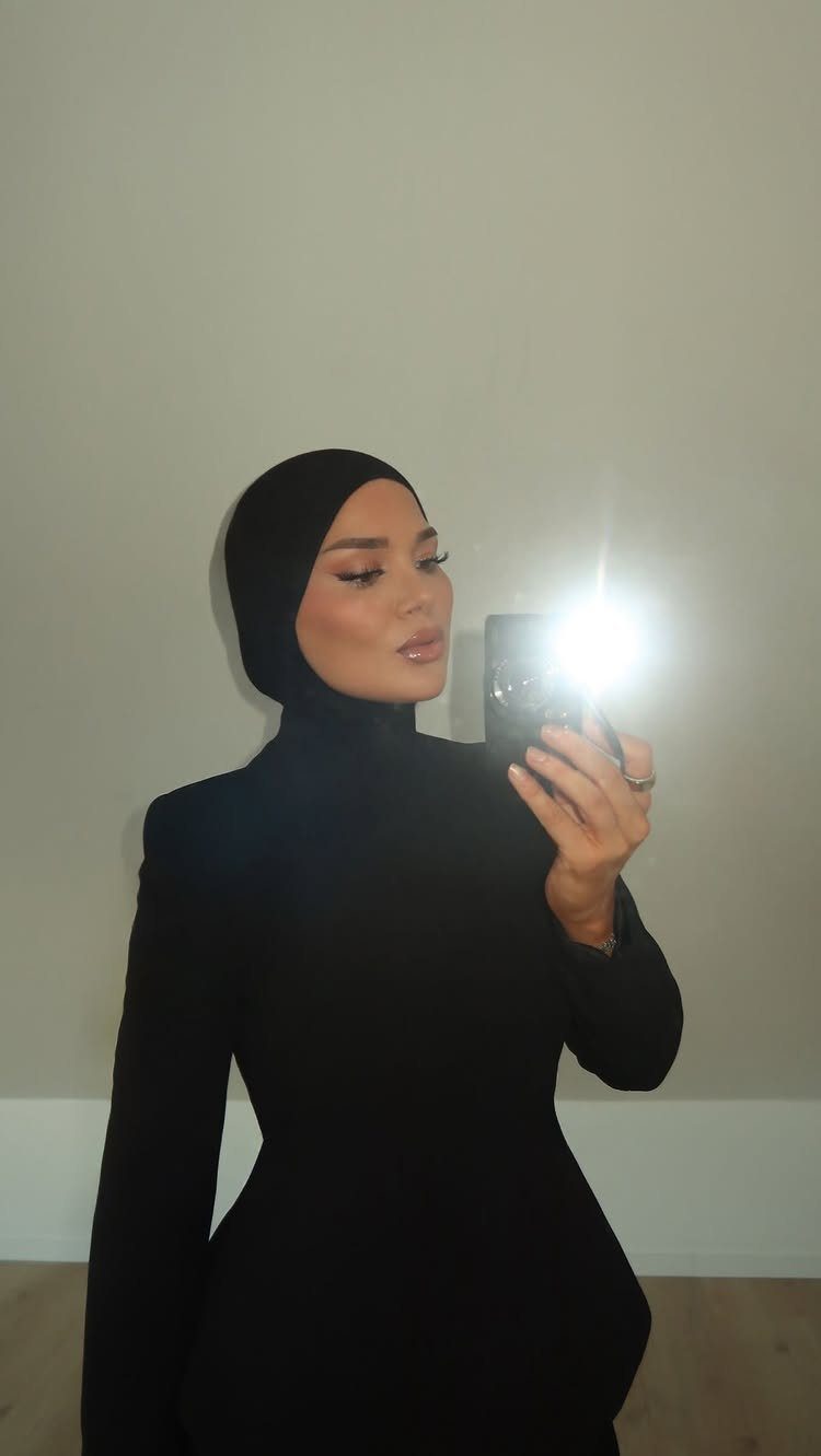 Woman in a black hijab and long-sleeved black dress taking a mirror selfie.