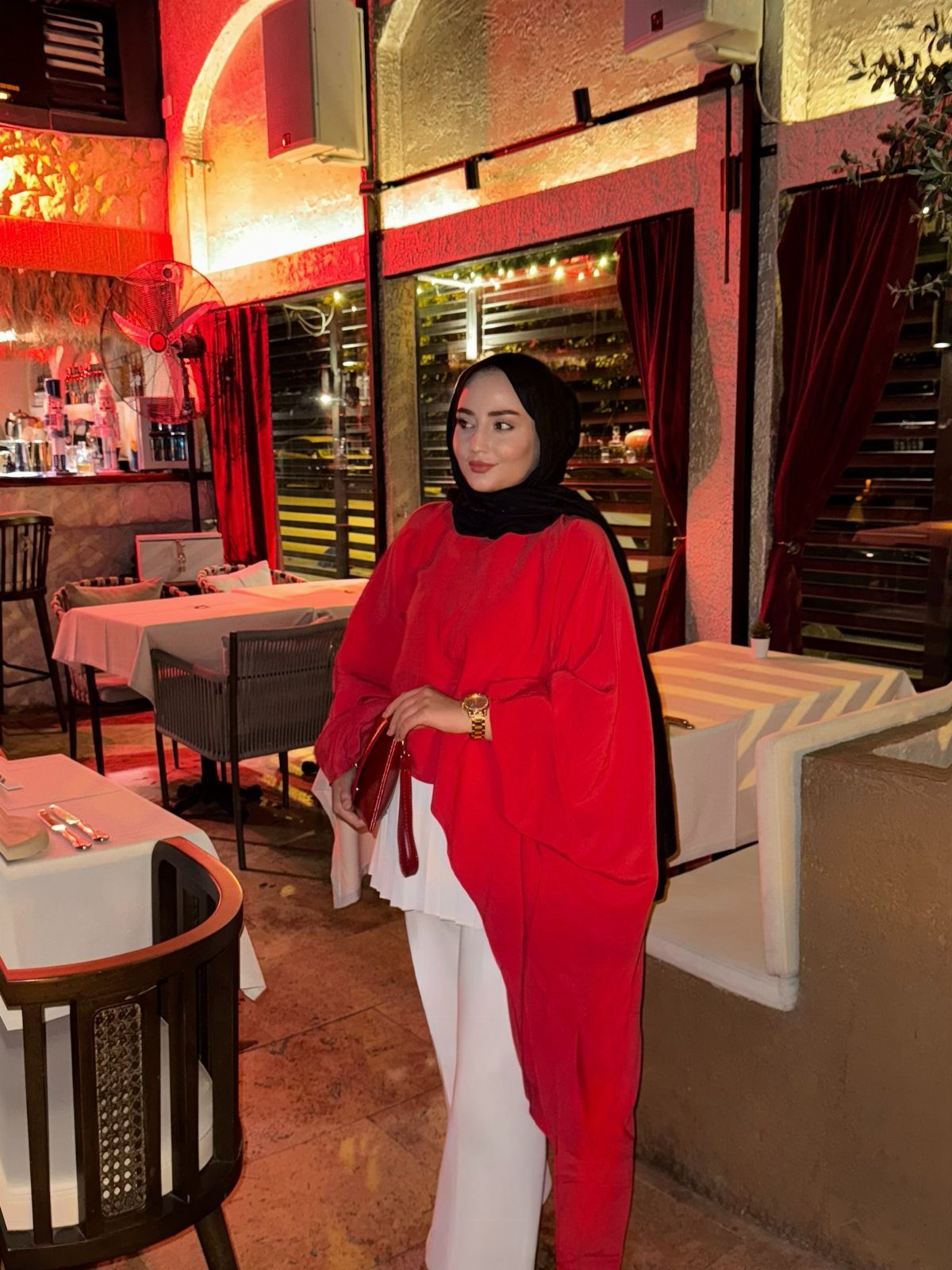Woman in red wrap top and white trousers posing in a restaurant